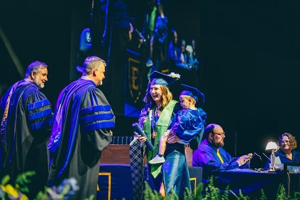 ETSU graduate celebrating on stage with a child at commencement
